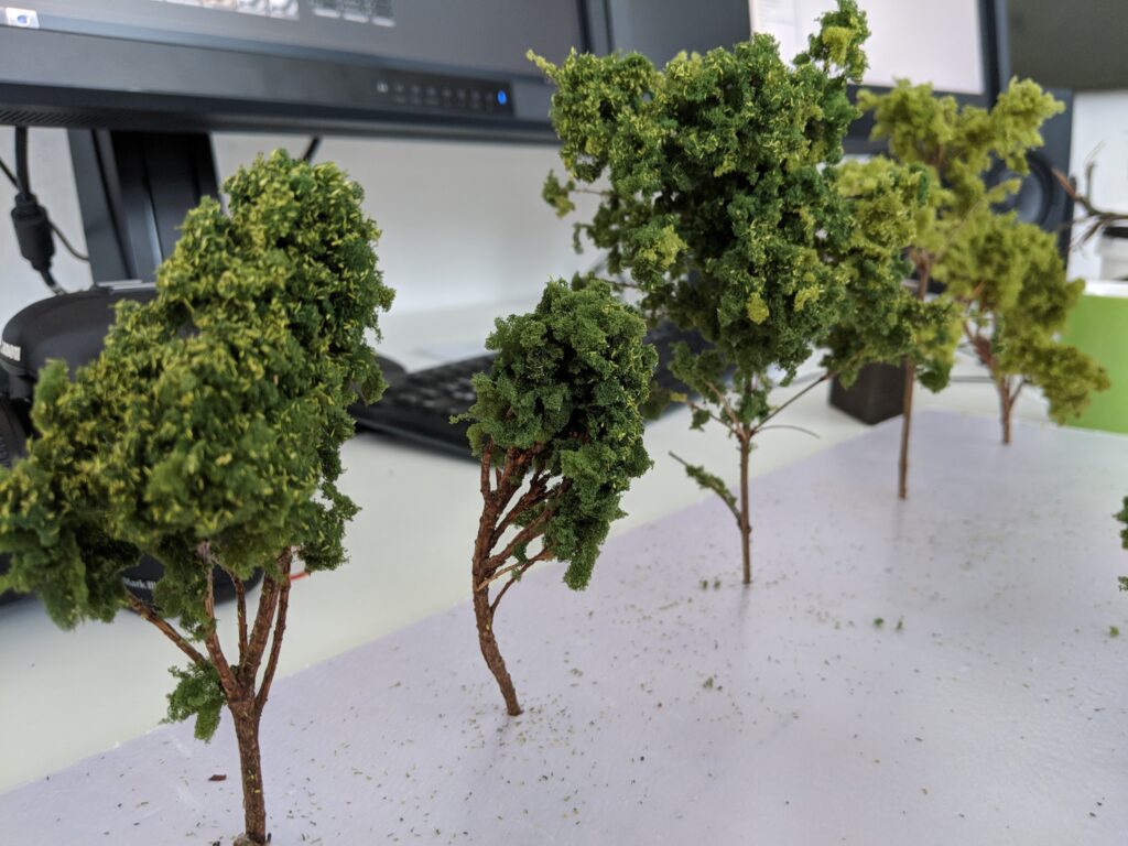 Modellbäume stehen auf der weißen Grundplatte einer Modelllandschaft