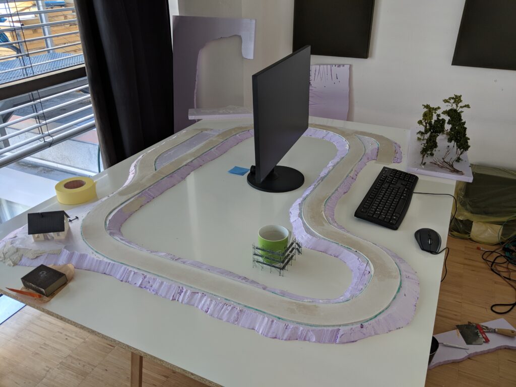 Weiße Modelllandschaft mit Straßen auf einem Schreibtisch im Studio, daneben Monitor und Tastatur