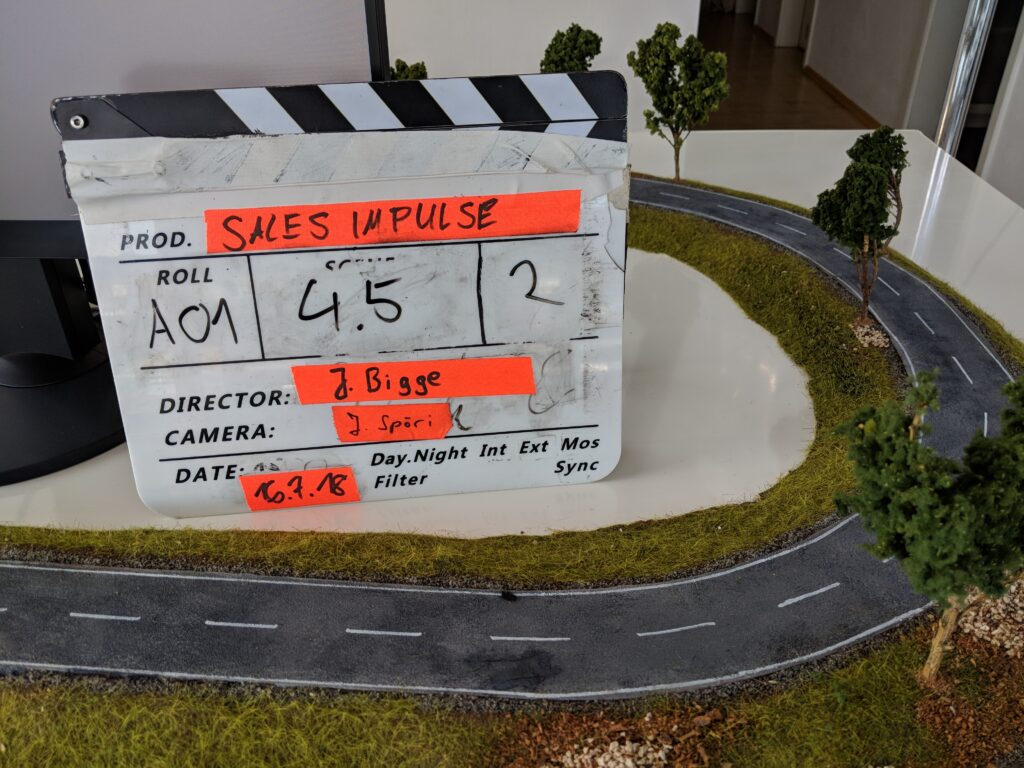 Filmklappe vor einer Modelllandschaft mit Straße und Grünflächen