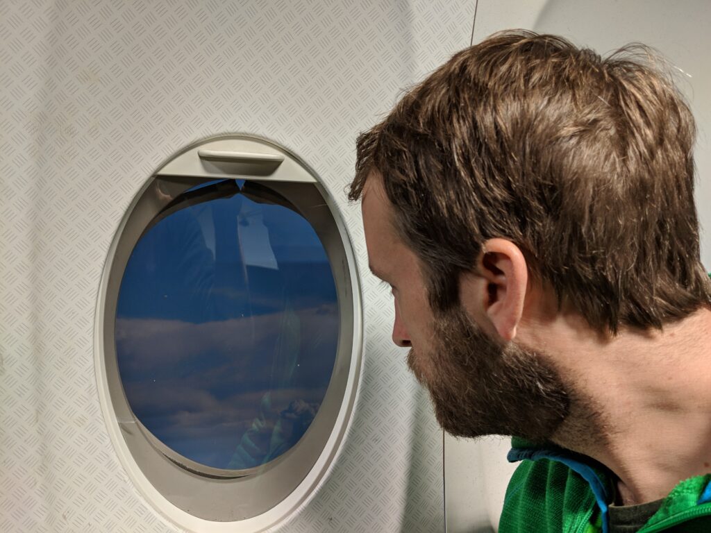 Darsteller blickt durch ein nachgebautes Flugzeugfenster am Set