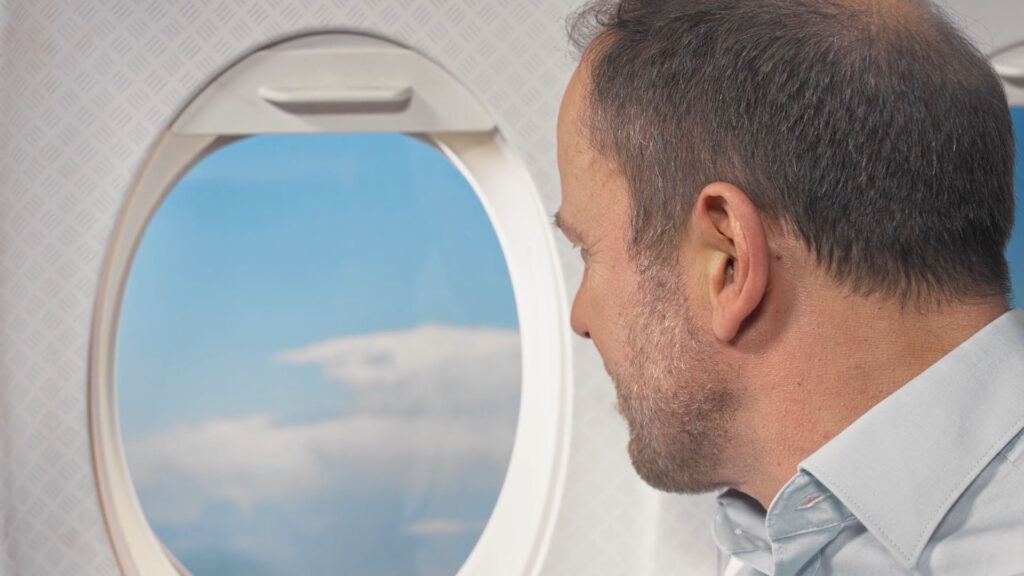 Mann blickt aus einem Flugzeugfenster in den Himmel