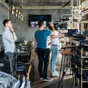 Videoproduktion Dreharbeiten eines Werbevideos in modernem Restaurant mit Kameramann, der Kamera auf Stativ bedient, und mehreren Personen im Hintergrund