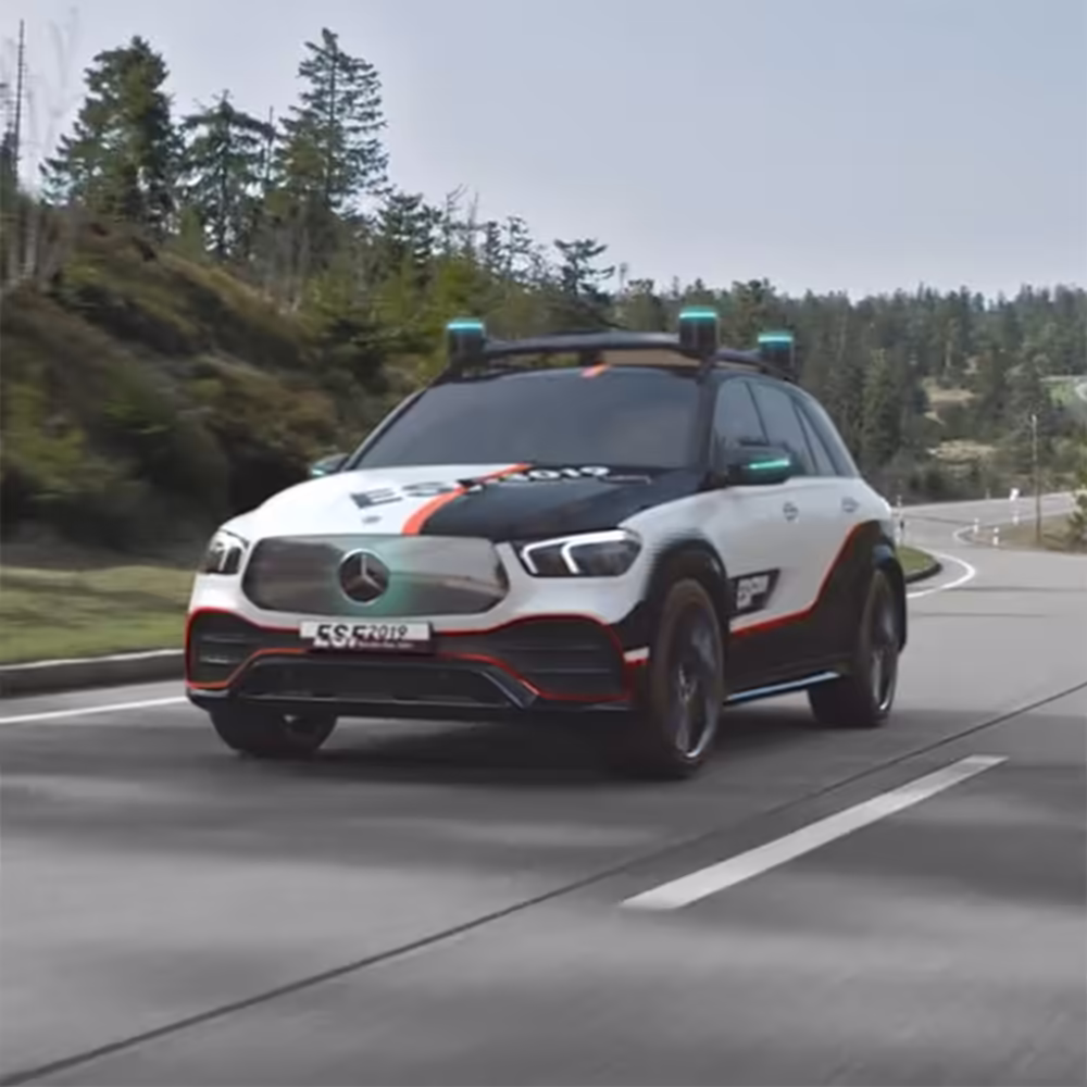 3D Rendering eines Mercedes-Benz SUV mit weiß-schwarzer Lackierung und orangen Akzenten, ausgestattet mit mehreren Sensoren auf dem Dach, fährt auf einer Landstraße mit Wald im Hintergrund.